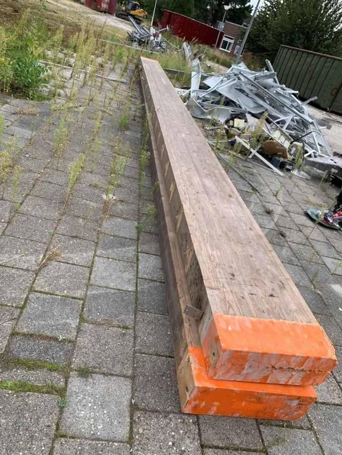 Twee houten balken op elkaar met oranje uiteinden op stoeptegels