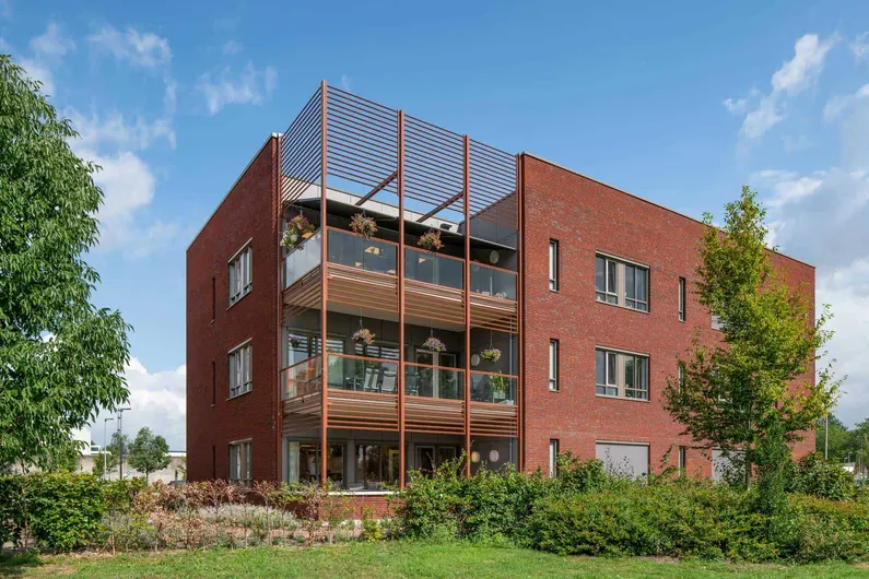 De hoek van het bakstenen gebouw met balkons met glas en planten