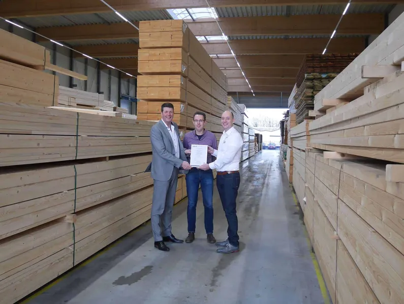 Drie mannen met een certificaat in de handen in een hal met allemaal houten palen