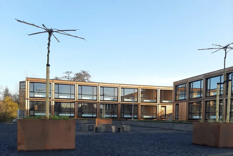 Houten gebouw met grote ramen met zwarte kozijnen en roestkleurige plantenbakken met kale bomen erin