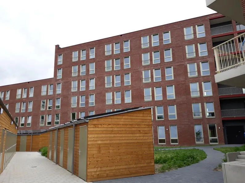 Bakstenen appartementengebouw met houten schuurtjes