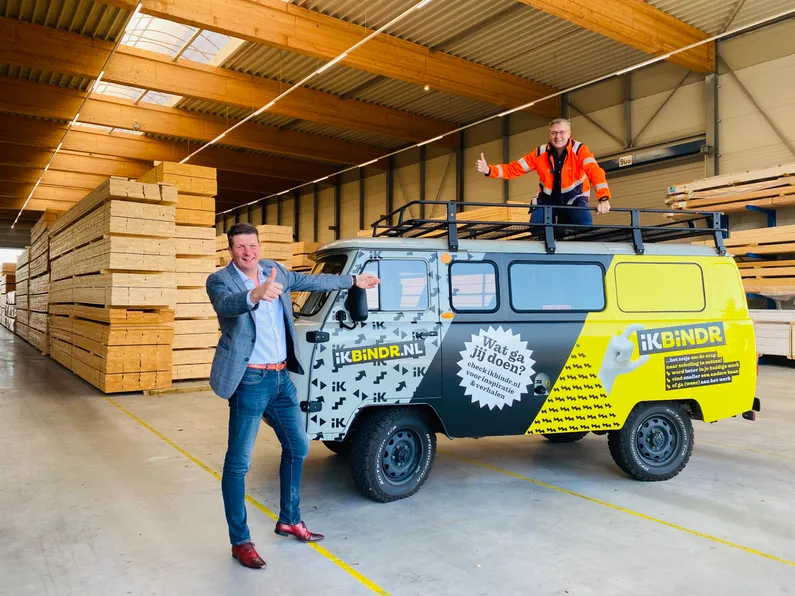 Een geel met zwart busje met 2 mannen in een hal met hout