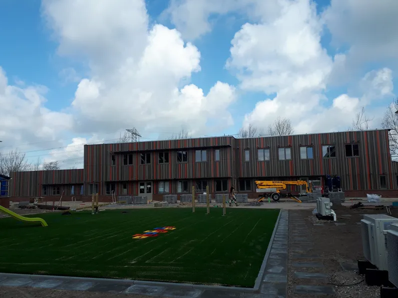 Rechthoekig gebouw met bruin en rode strepen met een grasveld ervoor