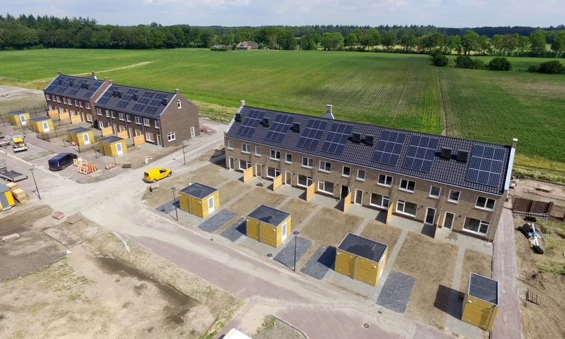 Nieuwbouwwijk met strakke, witte rijtjeshuizen met zwarte daken met zonnepanelen.