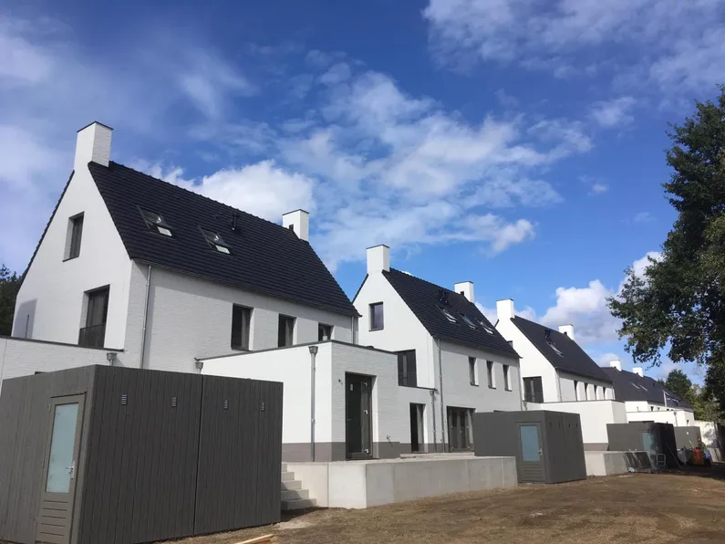 Witte twee-onder-een-kap huizen met zwart dak, grijze houten schuurtjes en een trappetje naar zand