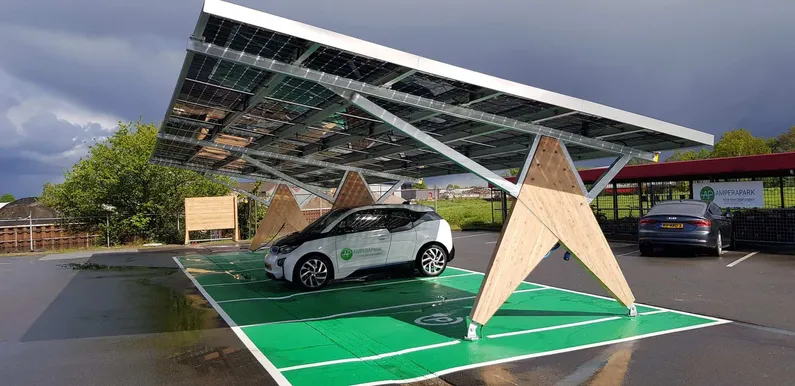 Houten constructie van overkapping met zonnepanelen met een vak van groen asfalt en witte auto