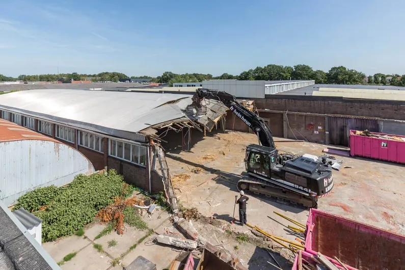 Bouwplaats met een kraan die een gebouw sloopt met roze containers